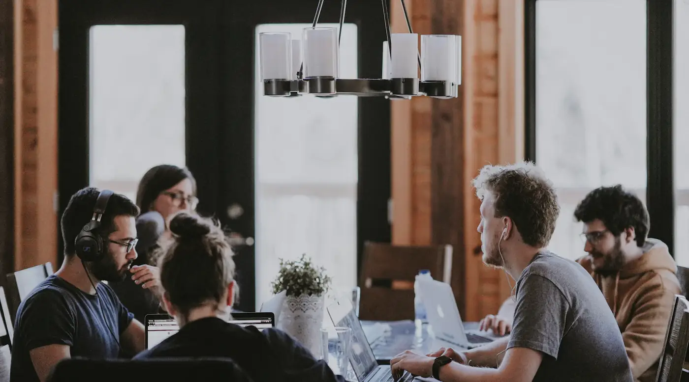 A small team talking around a table of laptops in a bright loft office