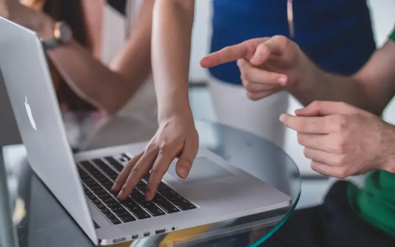 A senior engineer pointing at a junior colleague's laptop screen