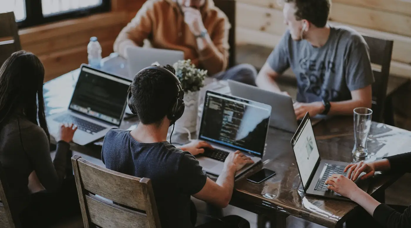 Engineers working side by side on laptops at a long wooden table